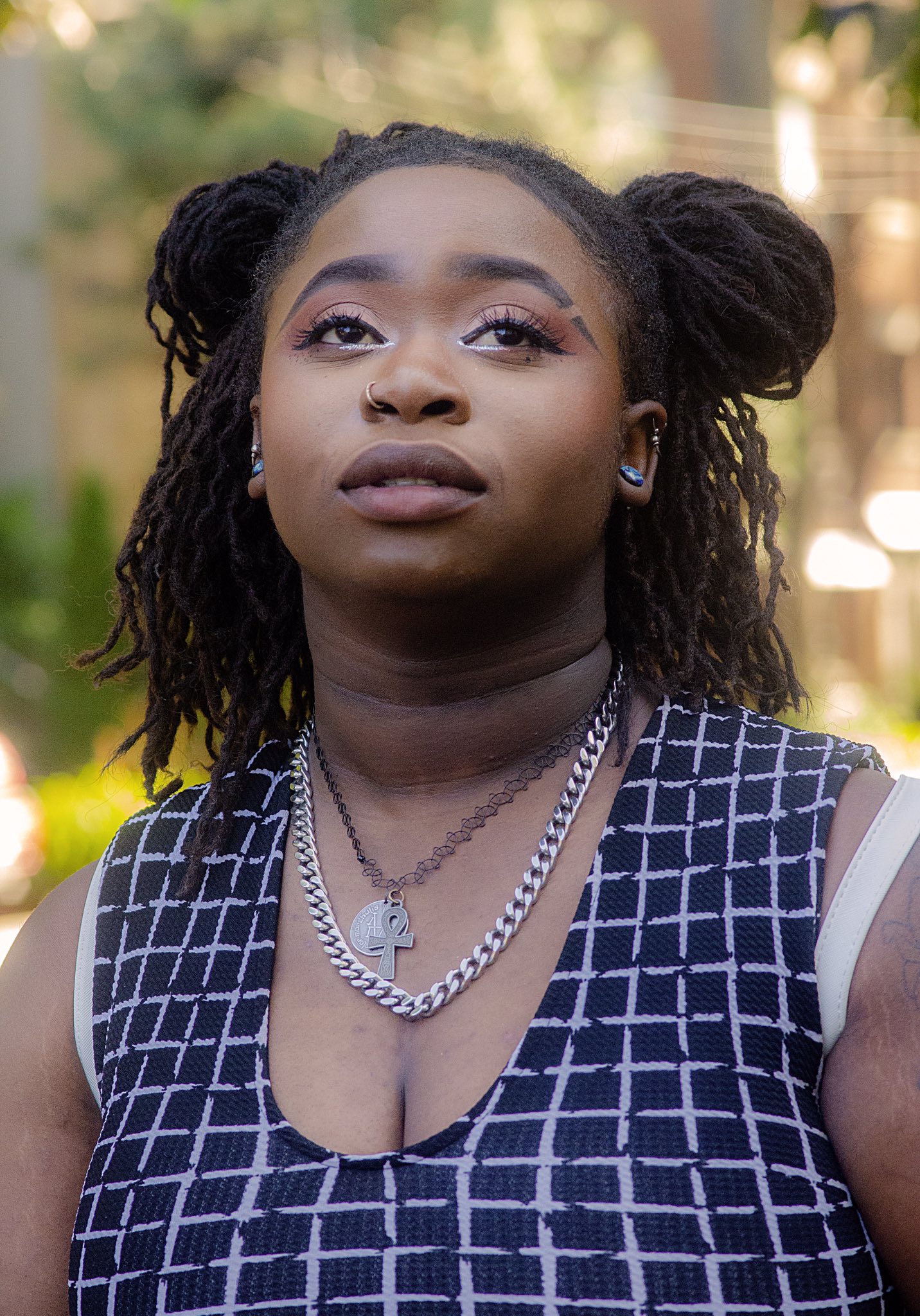 A woman of colour with loc’d hair styled in space buns gazes beyond the camera in a candid, thoughtful moment. Her expression captures a sense of calm and introspection.