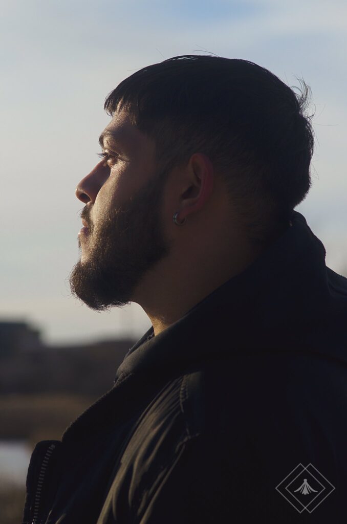 A close-up of a man of colour, his left profile captured against the backdrop of a clear blue sky, highlighting his features with a sense of calm and introspection.